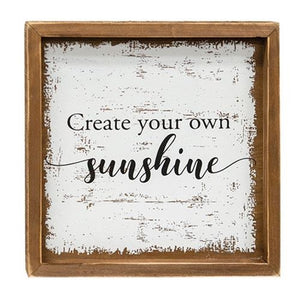 Rustic wood sign with brown mitered wood frame. Distressed white background with the inspirational quote "Create your own sunshine" in script.